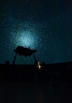 Planetarium Brussel beeld van de telescoop en sterren in de achtergrond in een groen-blauwe tint.